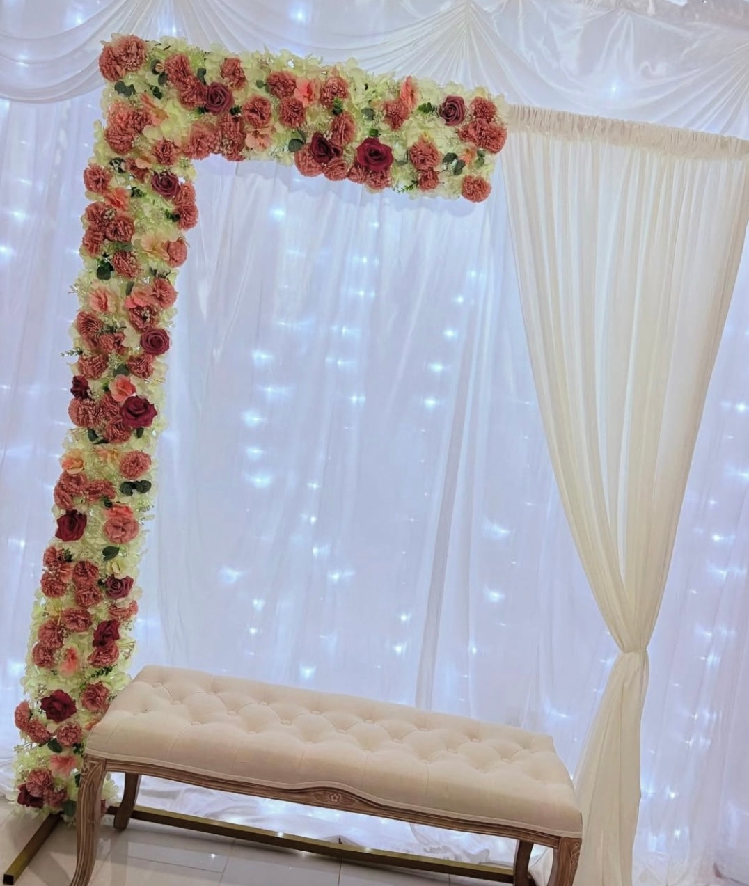Floral arch with a bench against a white curtain backdrop