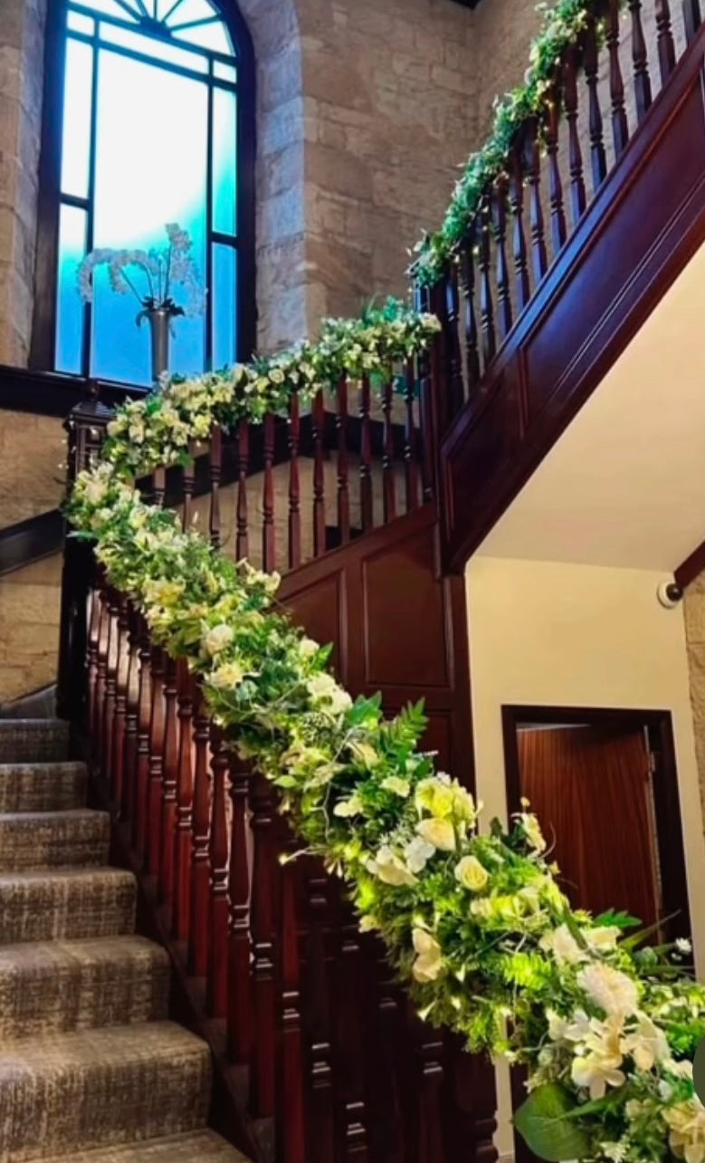 Decorative floral arrangement on a staircase railing in a building with large windows.